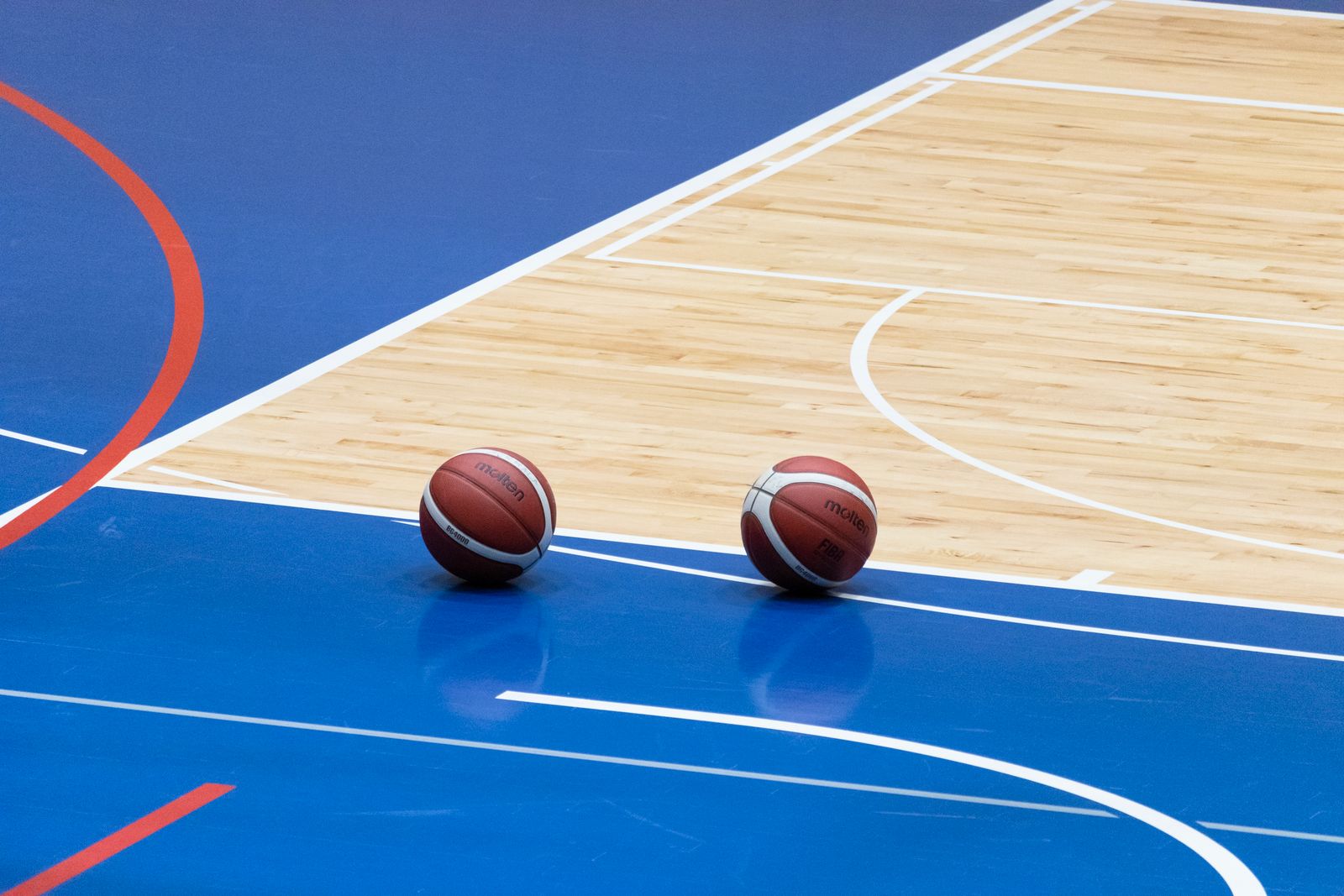 Two basketballs on an indoor hardwood and blue court