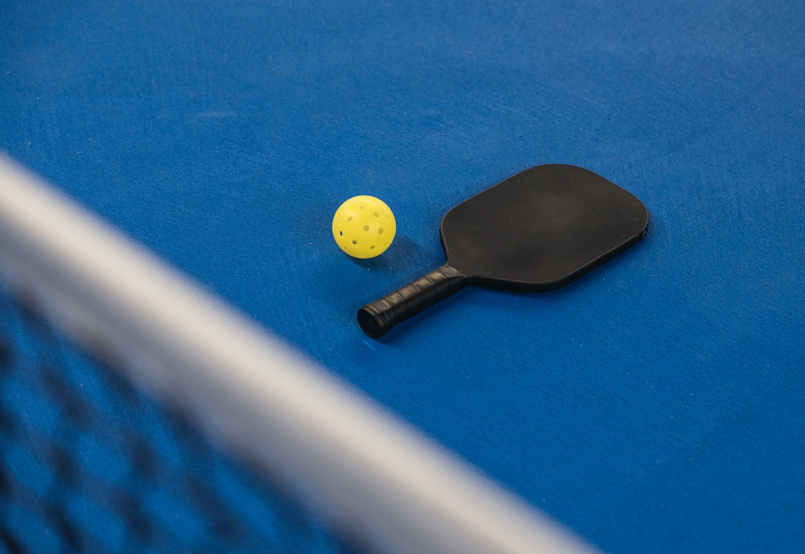 A pickleball paddle and ball on a blue court by the net